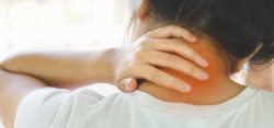A woman holding her hand to the back of her neck in pain