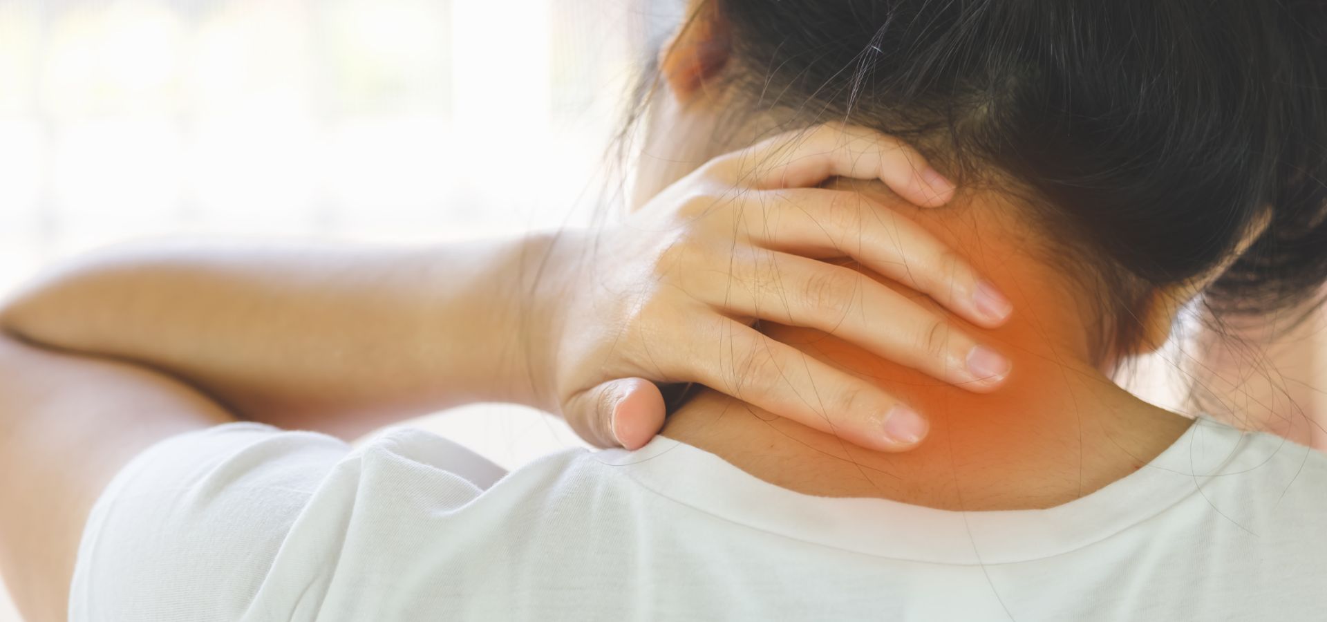 A woman holding her hand to the back of her neck in pain