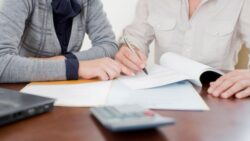 Two professional women signing paperwork at a desk