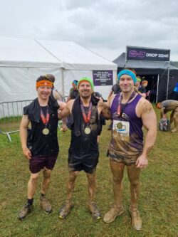Three men in running clothes after competing in muddy race