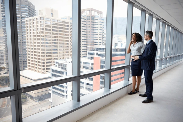 man and woman looking out of skyscraper window.
