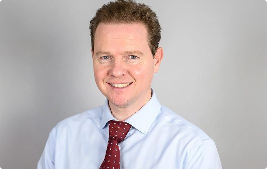 Smiling solicitor in a light blue shirt and red tie, representing the East Midlands legal firm Ellis-Fermor & Negus, known for family law, property law, and employment law.