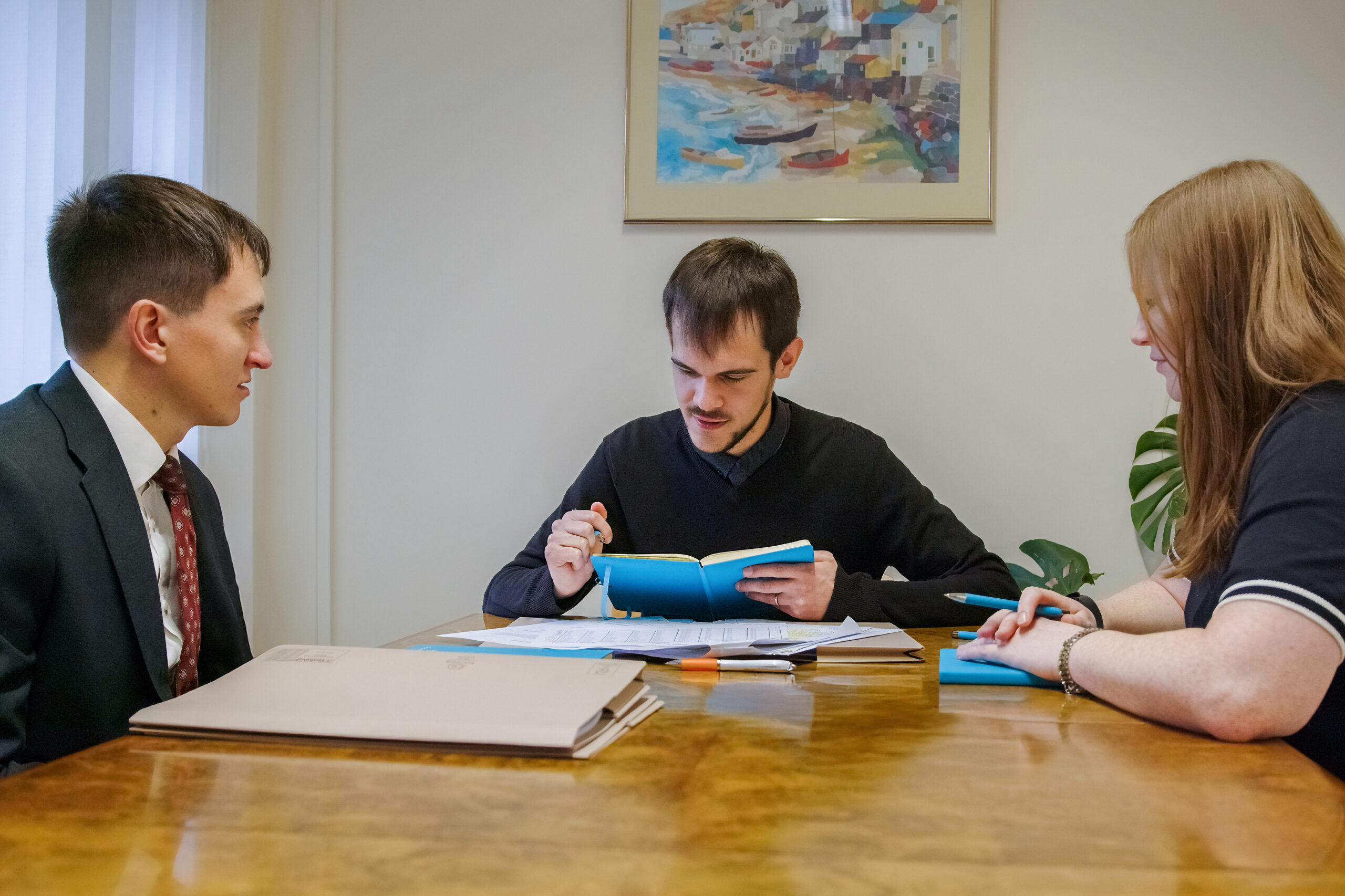 Three individuals engaged in a legal consultation at a meeting table, reviewing documents and discussing legal matters.