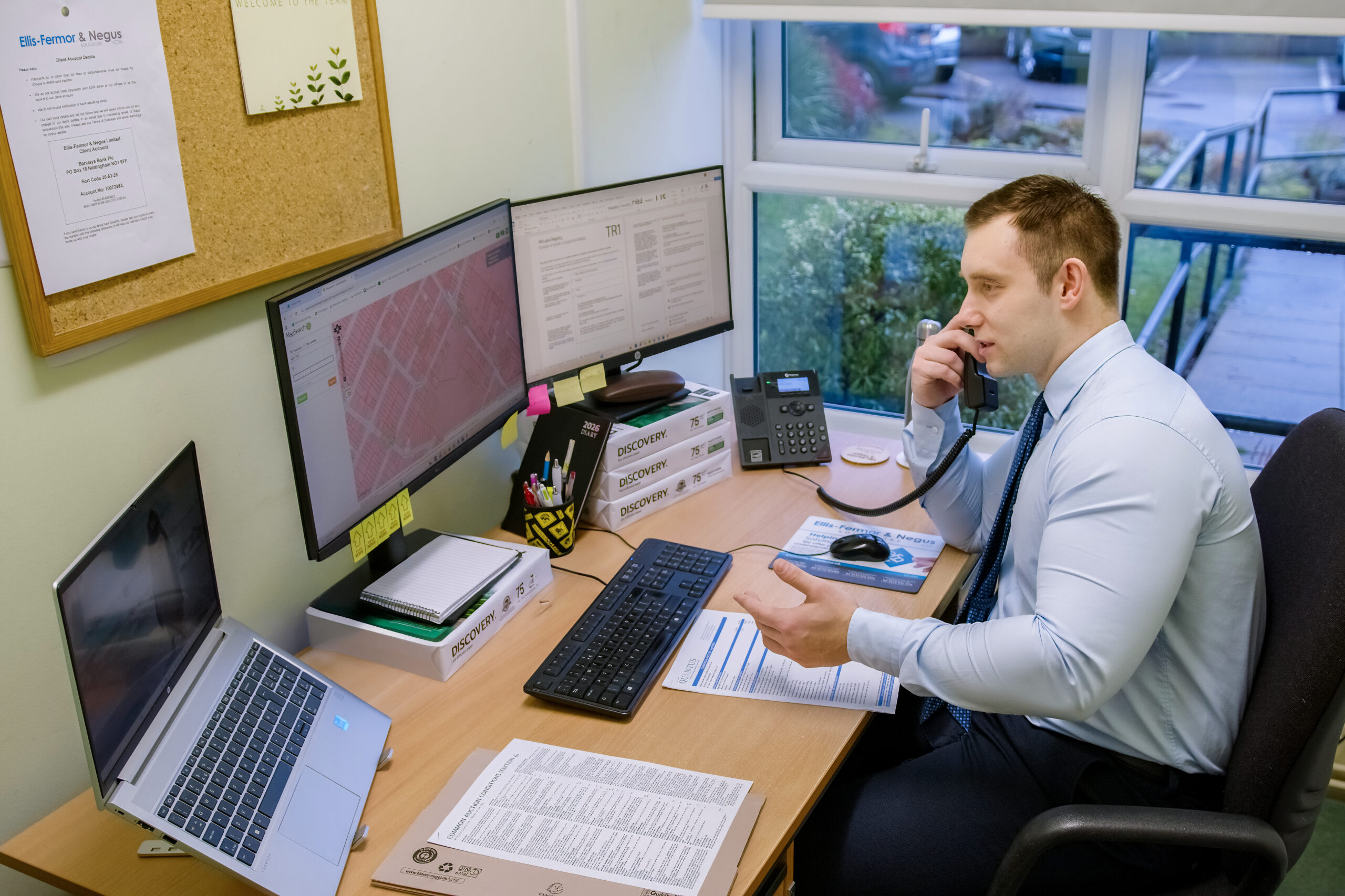 An East Midlands solicitor engaging in a phone conversation while working at a desk with multiple computer screens, emphasizing professional legal services.