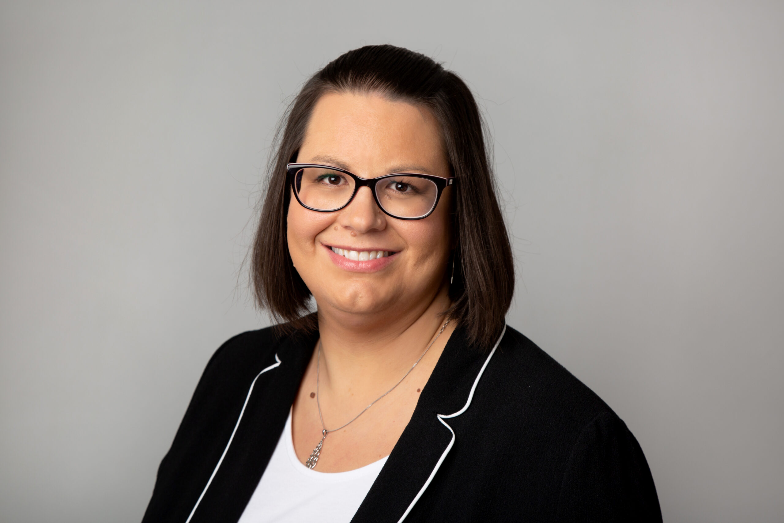 Headshot of a female solicitor with glasses, smiling, wearing a black blazer with white trim, representing legal services in the East Midlands.