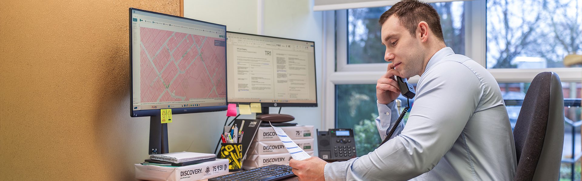 East Midlands solicitor providing legal advice over the phone while reviewing documents at a desk with computers and office supplies.